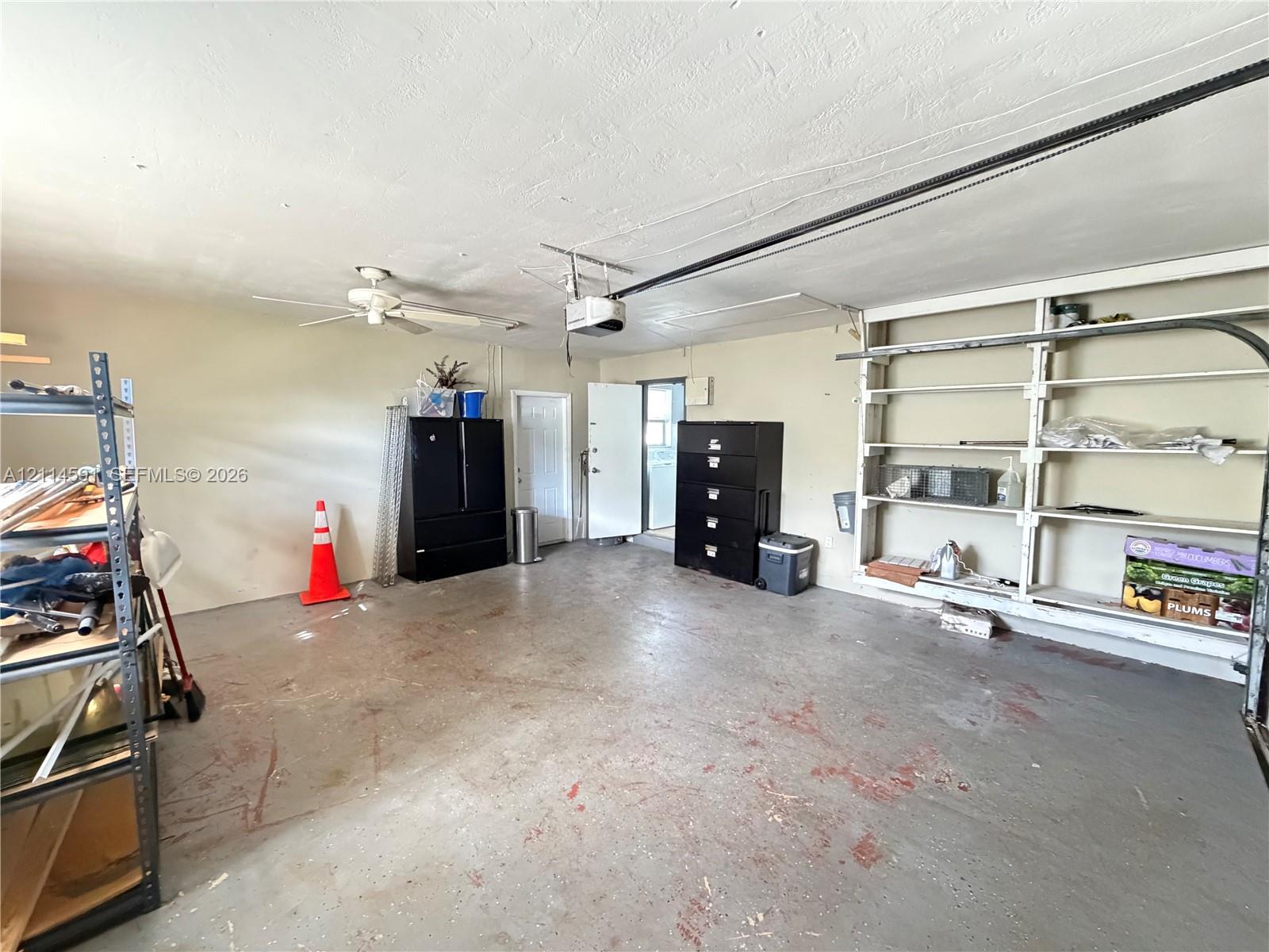 Attached garage featuring painted concrete flooring, ceiling-mounted light fixture with fan, and integrated wall-mounted storage shelving