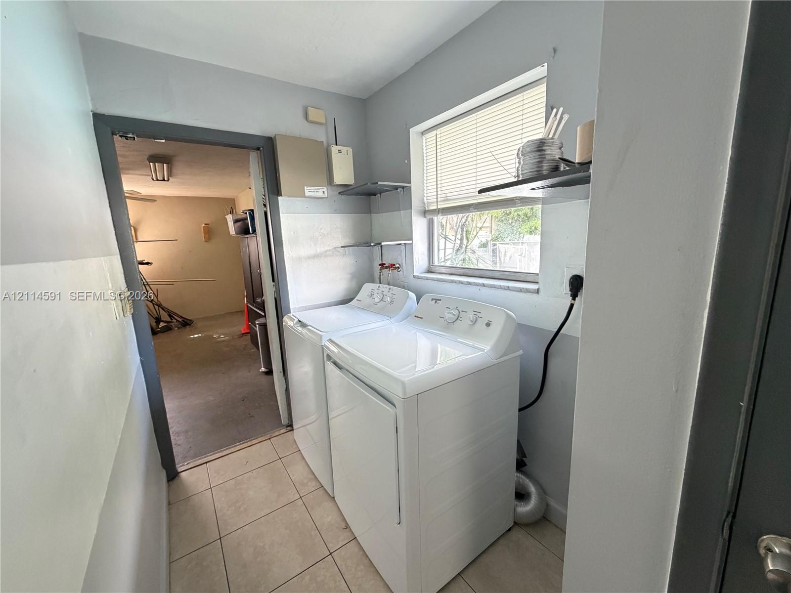Laundry area featuring tile flooring, a window, and wall-mounted shelving