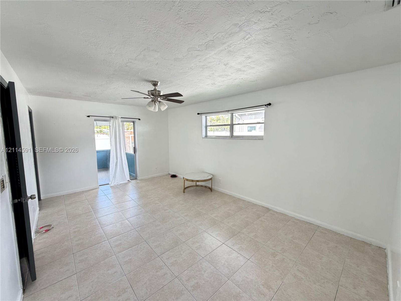 Interior room featuring large-format ceramic tile flooring, a multi-blade ceiling fan with integrated lighting, a rectangular single-hung window, and a sliding glass door