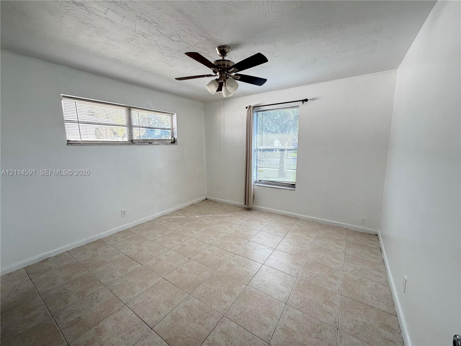 Neutral interior room featuring tile flooring, dual-pane windows, and a central ceiling fan with integrated lighting