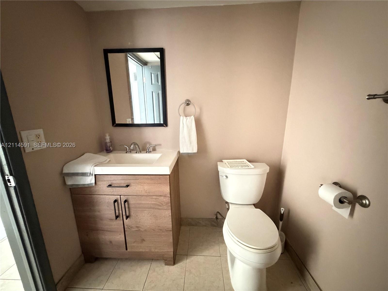 Wood-finish vanity cabinet with a rectangular sink, wall-mounted mirror with a dark frame, and tiled flooring