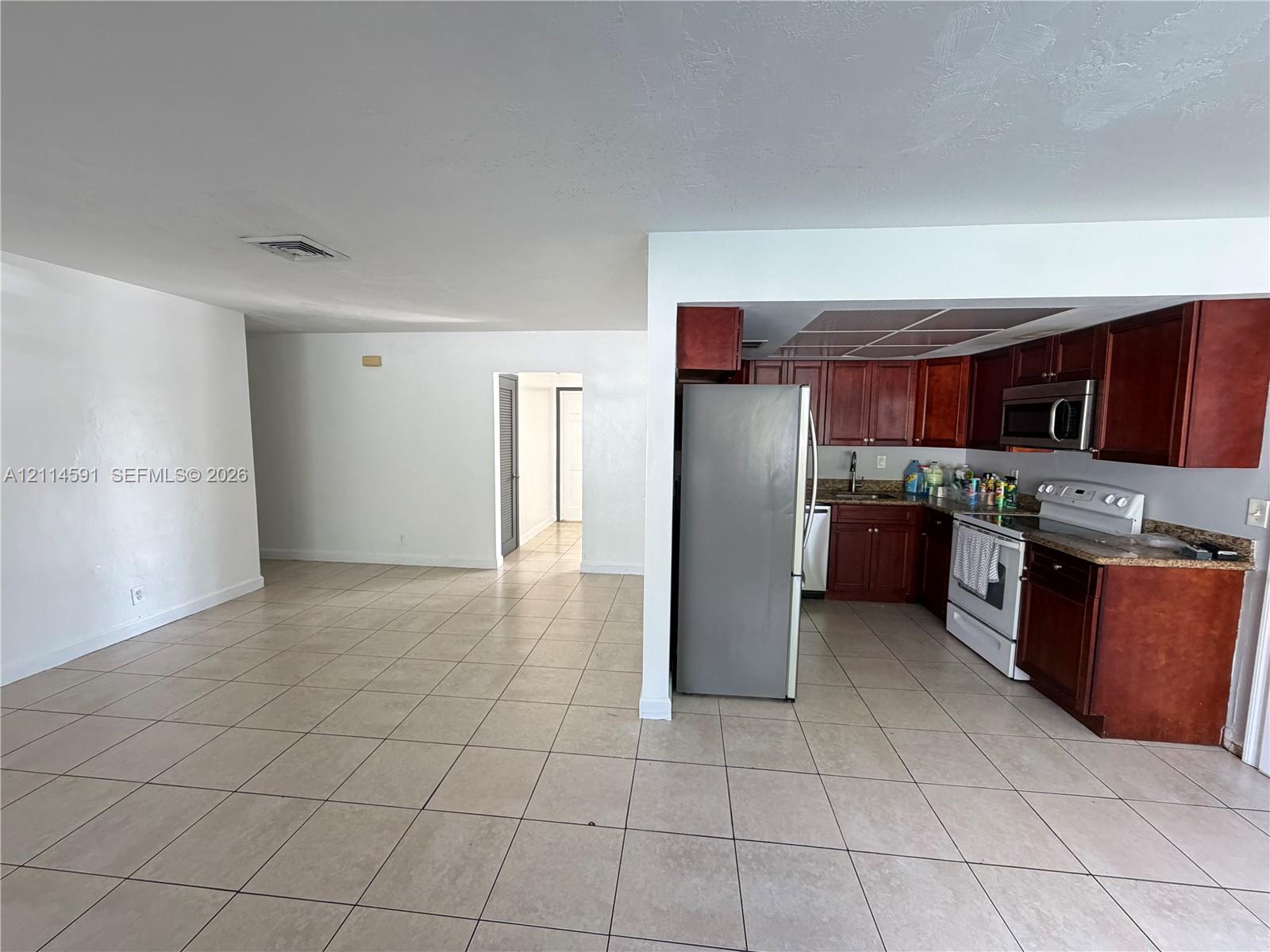 Kitchen featuring wood cabinetry, stone-finish countertops, and built-in appliances, accented by tile flooring throughout