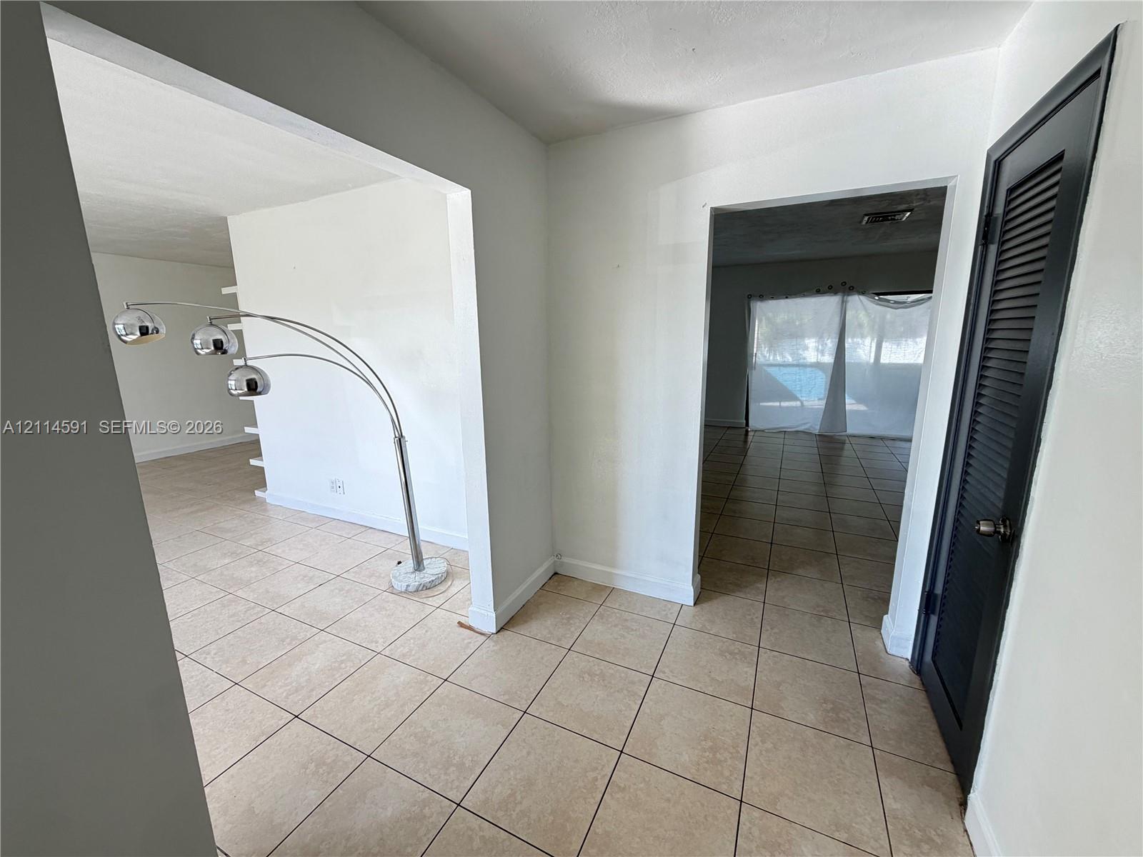 Interior space featuring neutral tile flooring, stark white walls, and a black louvered door