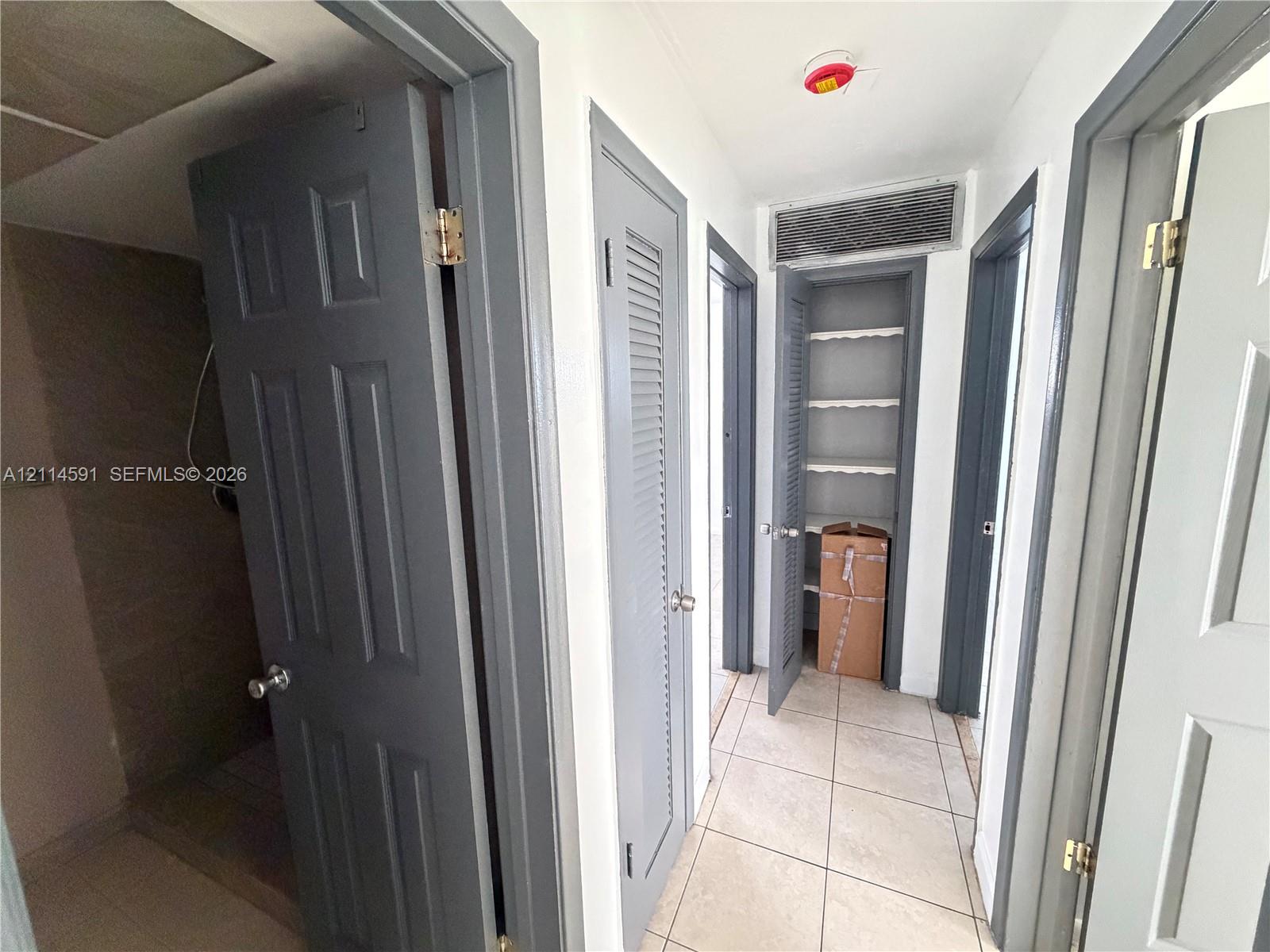 Hallway featuring large-format ceramic tile flooring, neutral wall paint, and multiple gray-painted interior doors