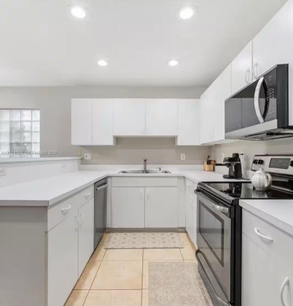 Kitchen featuring white cabinetry, solid-surface countertops, recessed ceiling lighting, a stainless steel over-the-range microwave, and ceramic tile flooring Kitchen featuring white cabinetry, solid-surface countertops, recessed ceiling lighting, a stainless steel over-the-range microwave, and ceramic tile flooring