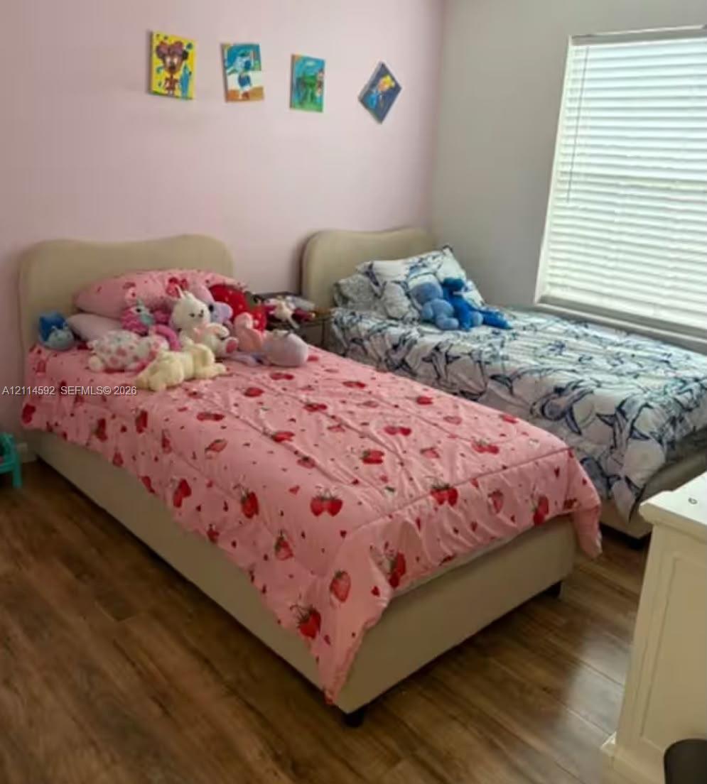Room featuring wood-finish flooring and a window equipped with horizontal blinds Room featuring wood-finish flooring and a window equipped with horizontal blinds