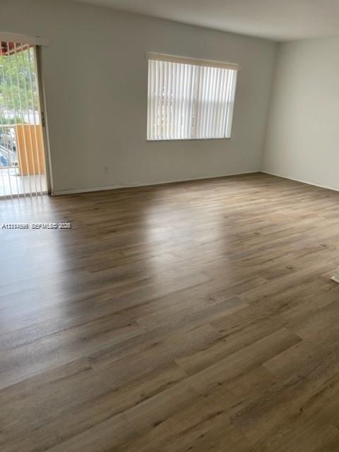 Interior space featuring wood-finish flooring, neutral wall paint, a window with vertical blinds, and a sliding glass door
