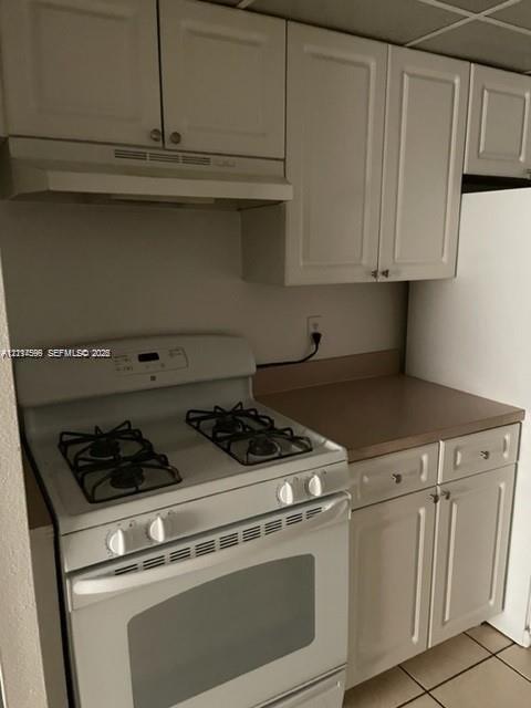 Kitchen area featuring white cabinetry, a white gas range with integrated vent hood, and solid-surface countertops
