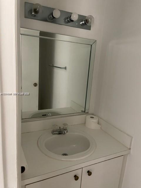 Built-in vanity featuring a white countertop with an integrated basin, four-light wall-mounted vanity fixture, and a square beveled-edge mirror