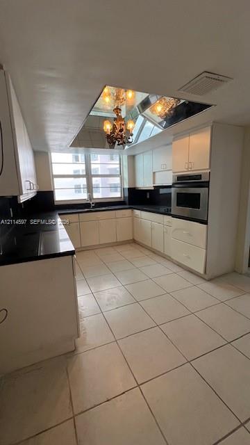 Kitchen featuring light-toned cabinetry, contrasting dark countertops, built-in wall oven, tiled flooring, and a mirrored ceiling element with integrated lighting