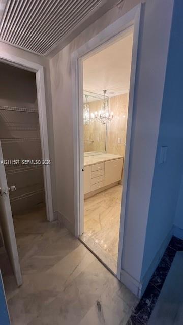 Storage closet featuring wire shelving and stone-finish tile flooring, leading to a bathroom with a vanity, stone-finish countertop, and decorative chandelier