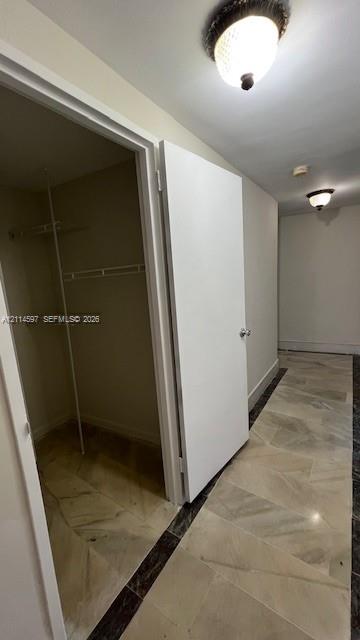 Hallway featuring stone tile flooring with decorative dark borders and flush-mount ceiling lighting, including a reach-in closet with built-in metal shelving