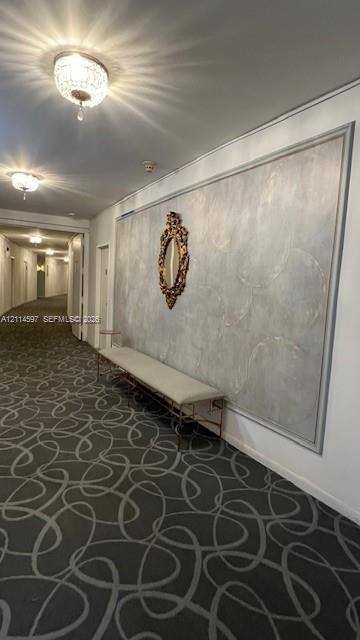 Hallway featuring patterned wall-to-wall carpeting, decorative ceiling-mounted crystal fixtures, and a recessed wall panel with textured finish Hallway featuring patterned wall-to-wall carpeting, decorative ceiling-mounted crystal fixtures, and a recessed wall panel with textured finish