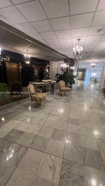 Large-format stone flooring, wall-spanning mirror, and multi-arm chandelier fixtures in a high-ceiling lobby Large-format stone flooring, wall-spanning mirror, and multi-arm chandelier fixtures in a high-ceiling lobby