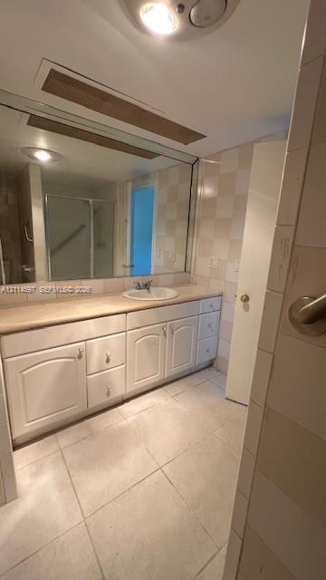 Bathroom featuring a large vanity with white cabinetry, integrated sink, and stone-surface countertop, complemented by floor-to-ceiling wall tiles and ceramic floor tiling