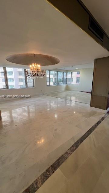 Polished stone flooring with decorative inlay, expansive floor-to-ceiling windows, recessed circular ceiling feature, and a crystal chandelier