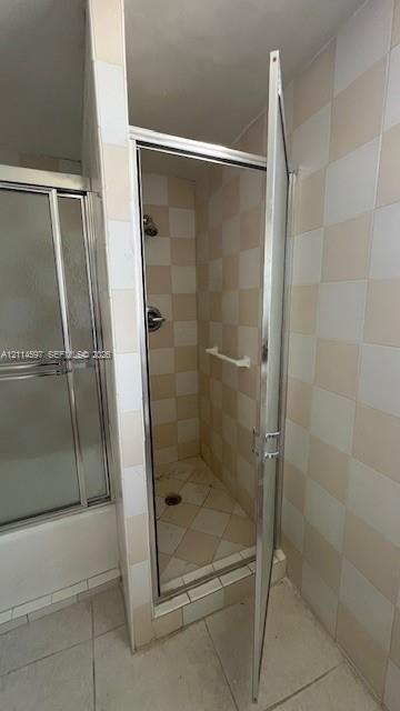Walk-in shower enclosure featuring a chrome-framed hinged door, wall-mounted shower head, integrated towel bar, and checkerboard-patterned tile wall surfacing