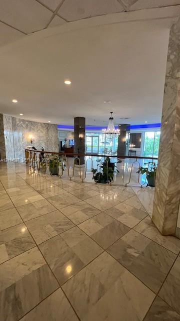 Polished stone flooring throughout, expansive wall-to-wall stone cladding, central chandelier, and decorative metal balustrade with a wooden handrail Polished stone flooring throughout, expansive wall-to-wall stone cladding, central chandelier, and decorative metal balustrade with a wooden handrail