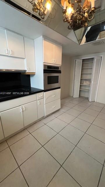 Kitchen featuring white cabinetry, dark countertops, built-in stainless steel double oven, tile flooring, and mirrored ceiling detailing