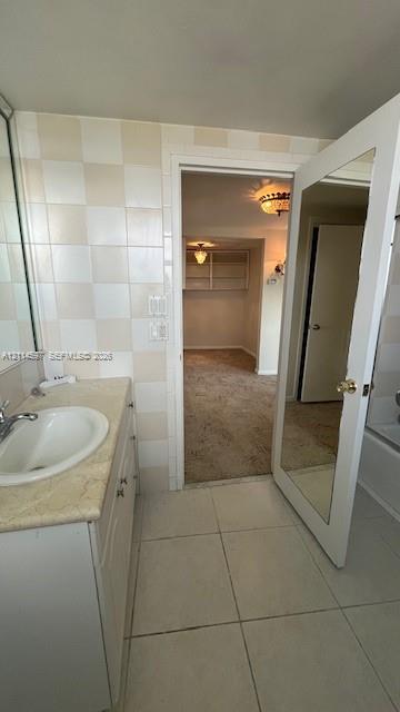 Bathroom featuring a vanity with an integrated basin, neutral stone-finish countertop, full-height wall tiling, and a door with an inset full-length mirror