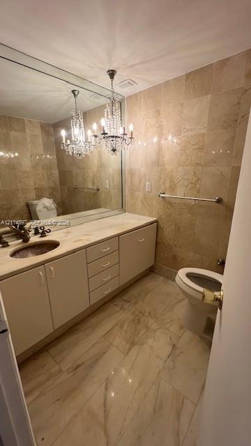 Bathroom featuring full-wall tile surround, vanity with inset sink and stone countertop, large-format tiled flooring, and a decorative crystal chandelier
