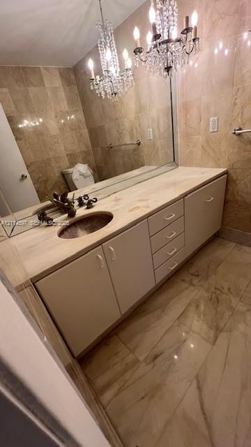 Bathroom vanity with a stone countertop, integrated oval sink, multi-drawer cabinetry, full-wall mirror, and dual crystal chandeliers