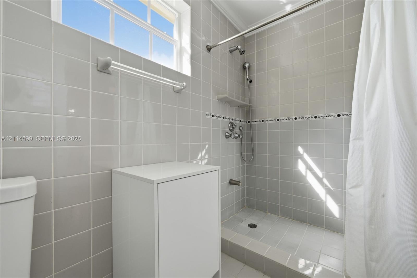 Full-height neutral wall tiling featuring a decorative accent border, walk-in shower with handheld showerhead, transom window, and integrated shelving