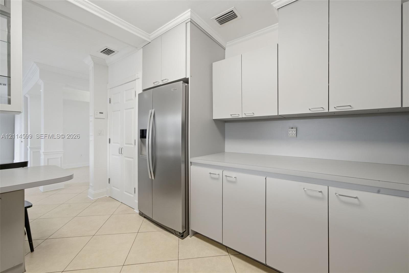 Kitchen featuring light-toned cabinetry, stainless steel side-by-side refrigerator, expansive solid-surface countertop, and ceramic tile flooring