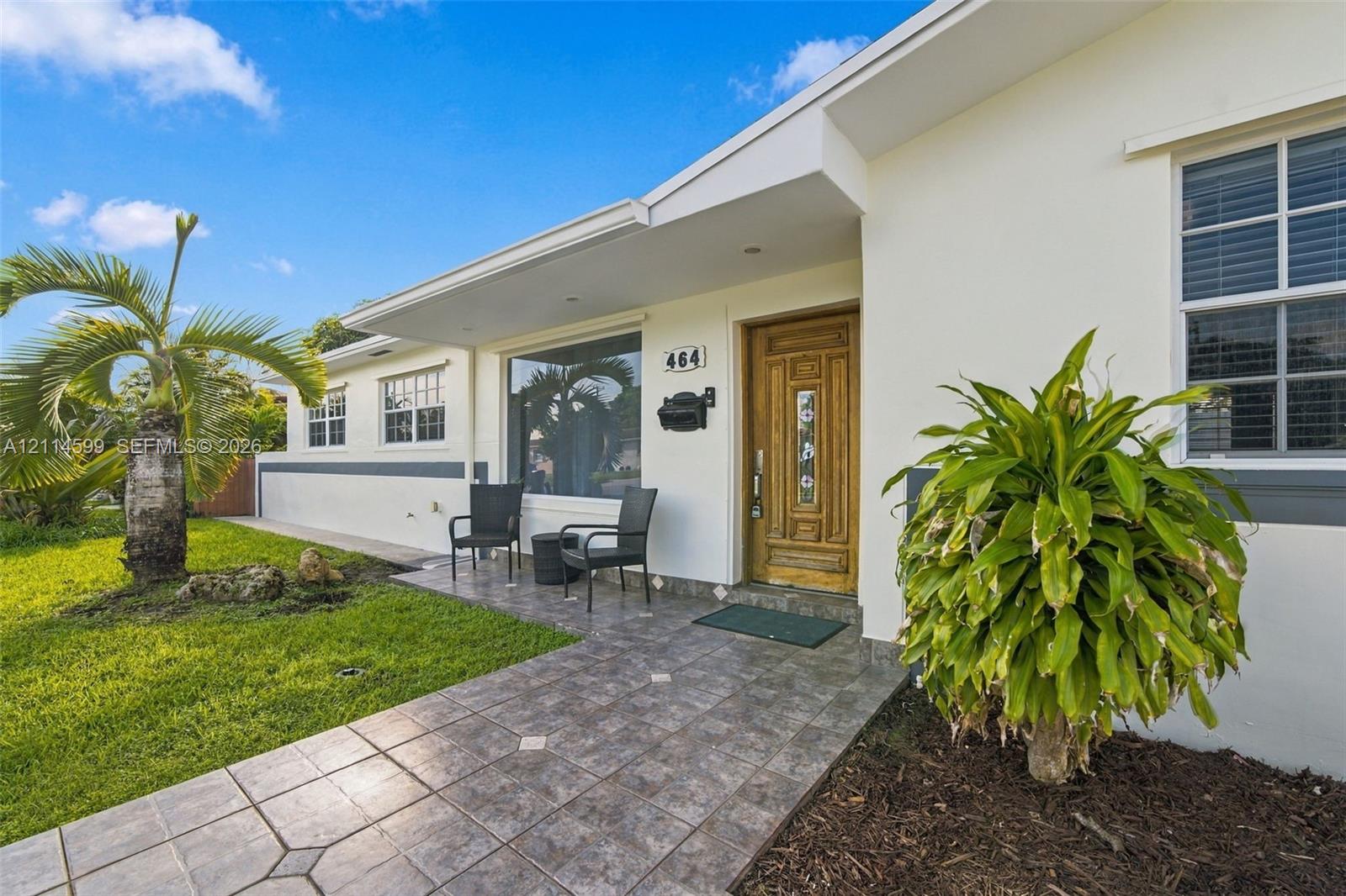 Exterior featuring a stucco facade, a decorative wood-finish entry door with inset glass detailing, multi-pane windows, and a tiled walkway