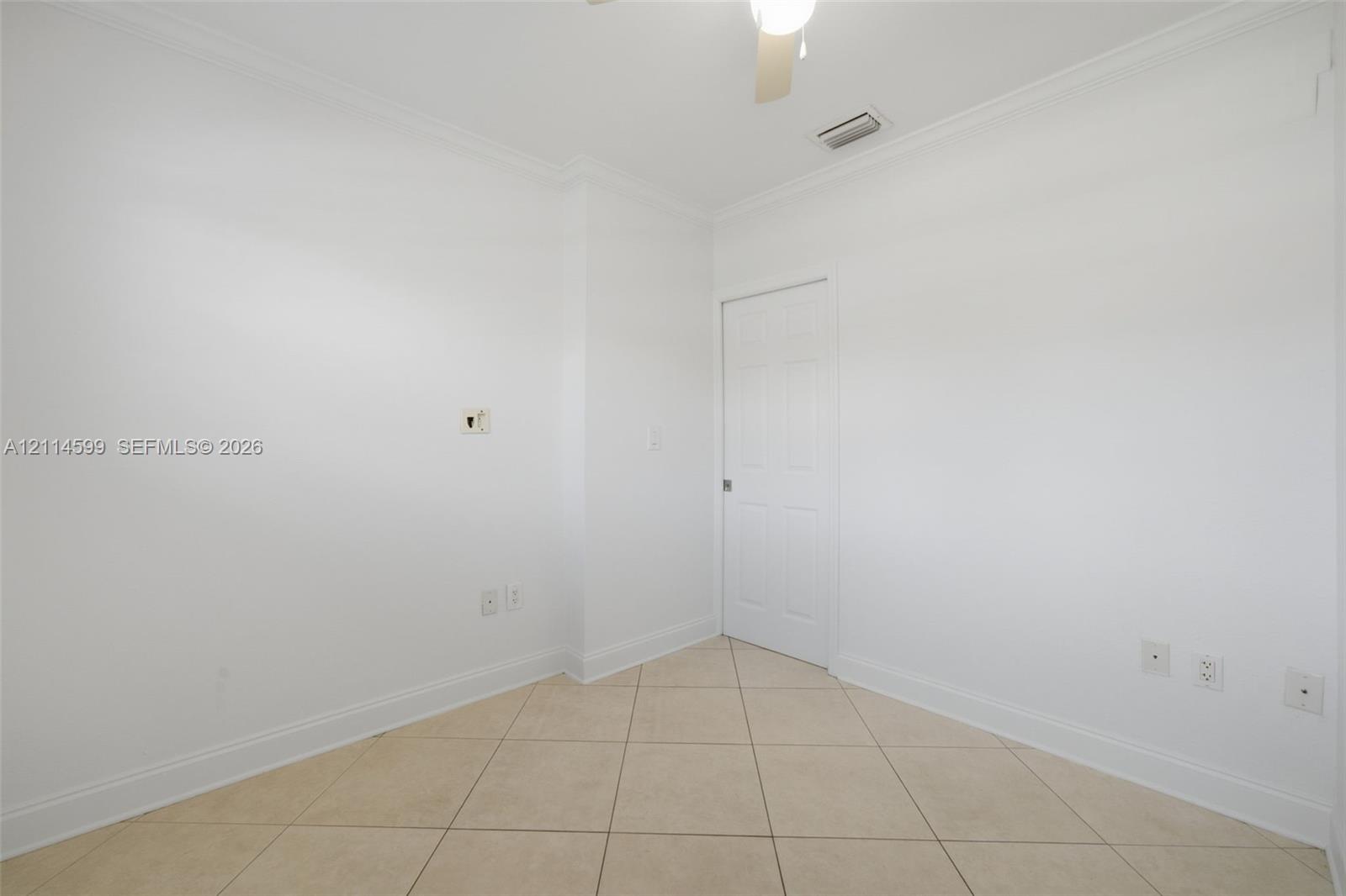 Interior room featuring neutral ceramic tile flooring, crown molding, a six-panel door, and a ceiling-mounted light fixture
