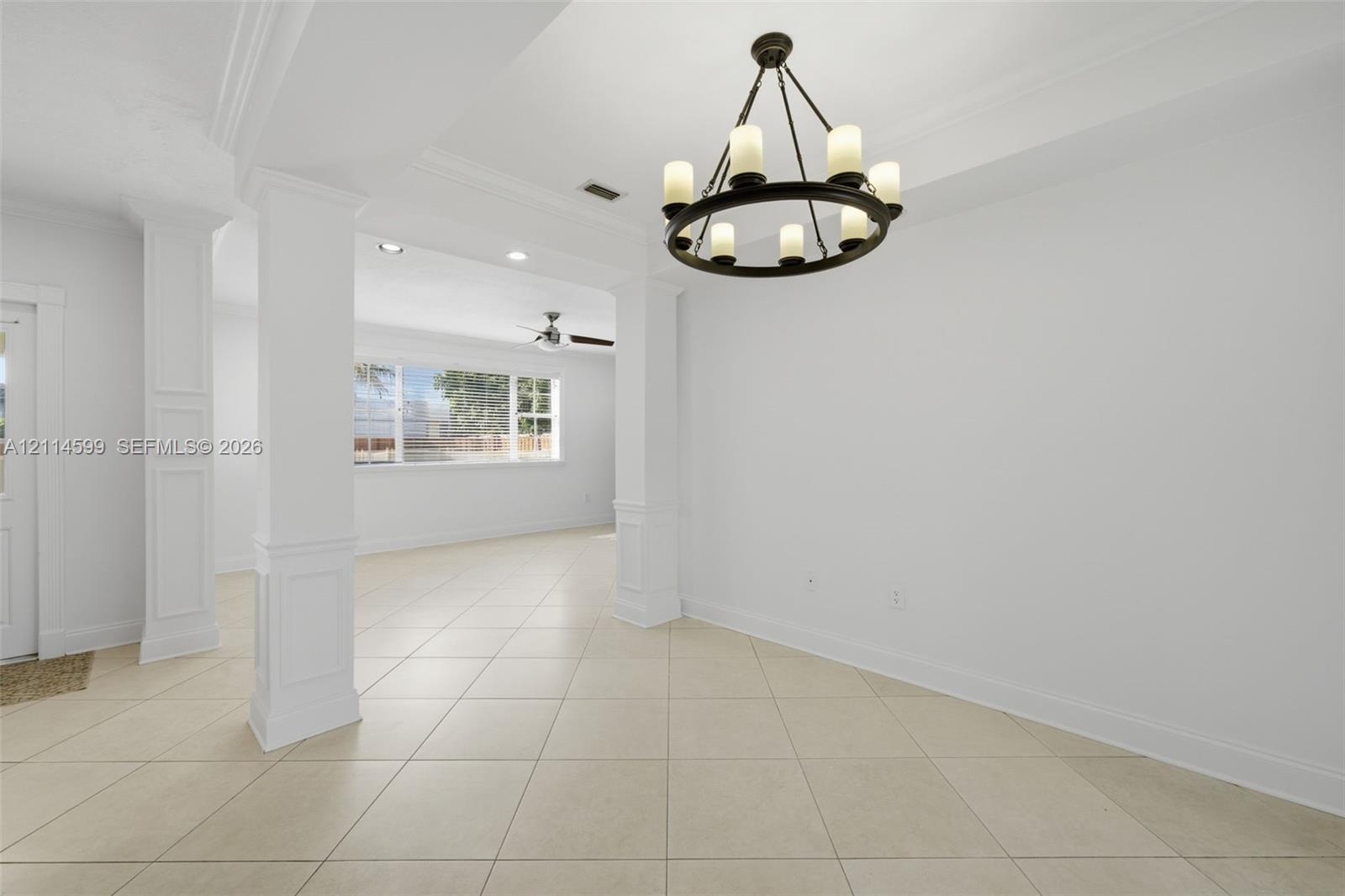 Open floor plan interior featuring tile flooring, crown molding, square columns with wainscoting detail, and a six-light circular chandelier