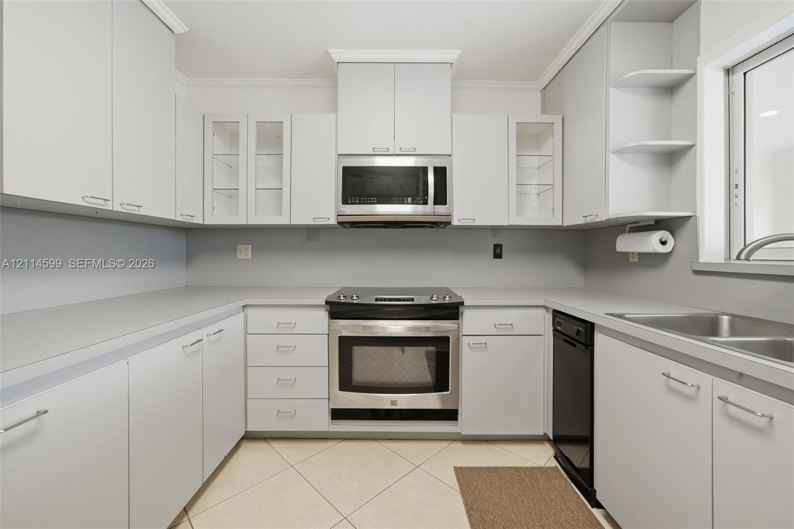 Kitchen featuring light-toned cabinetry with glass-front display panels, stainless steel appliances, open shelving, a double-basin stainless steel sink, and tile flooring