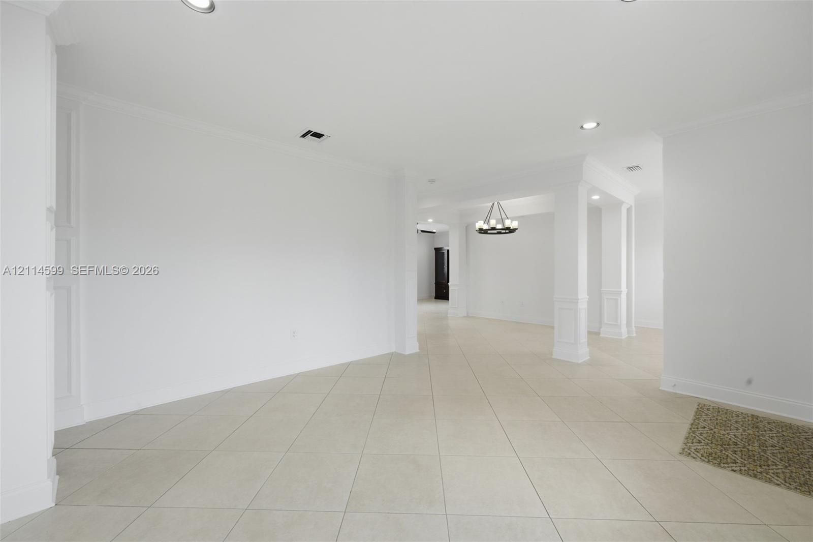 Open floor plan featuring large-format ceramic tile flooring, recessed lighting, architectural columns with wainscoting detail, and a multi-light chandelier