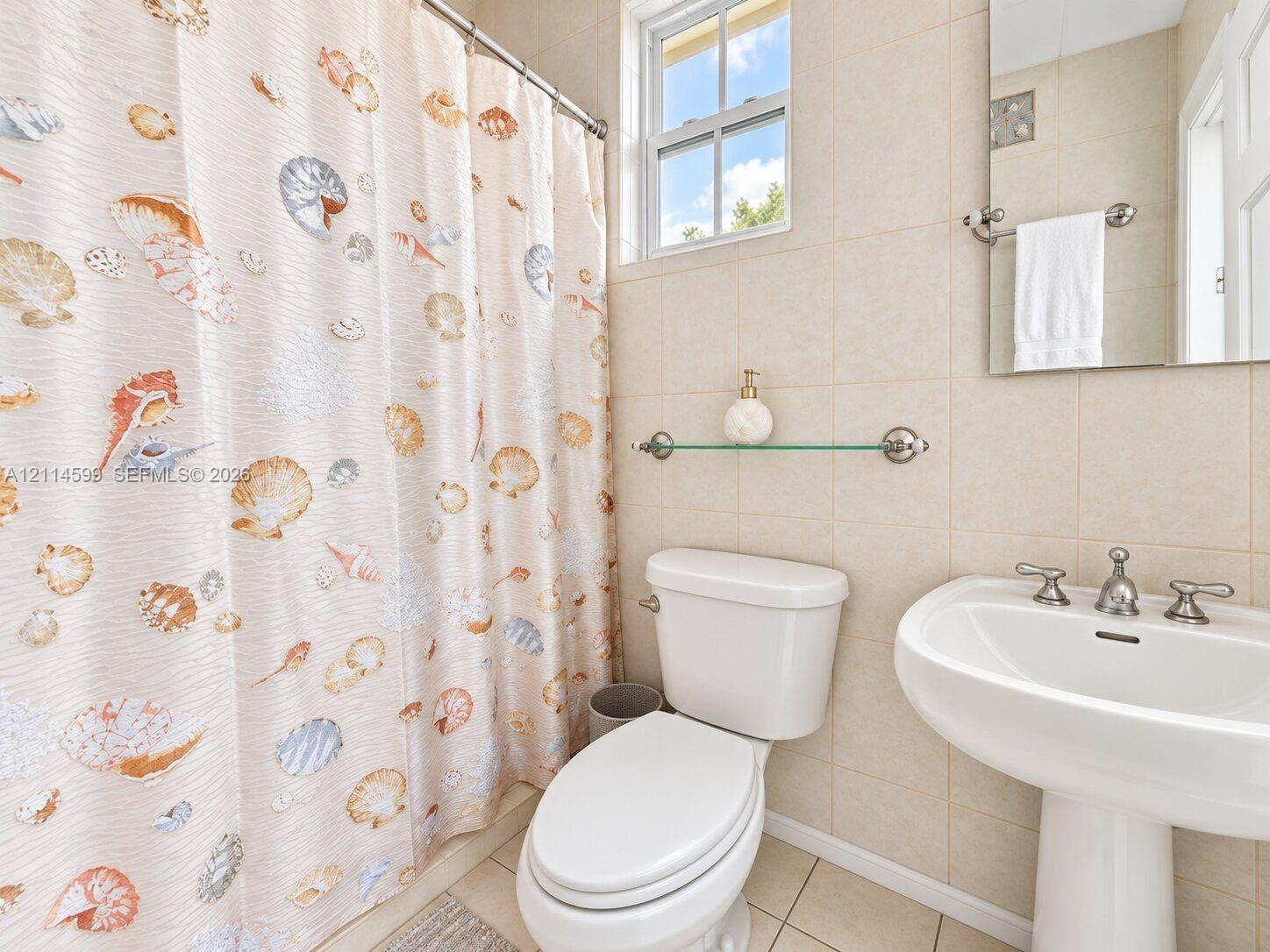 Wall-mounted glass shelving, porcelain pedestal sink with polished chrome widespread faucet, frameless rectangular mirror, light-toned ceramic wall tile, and double-hung window
