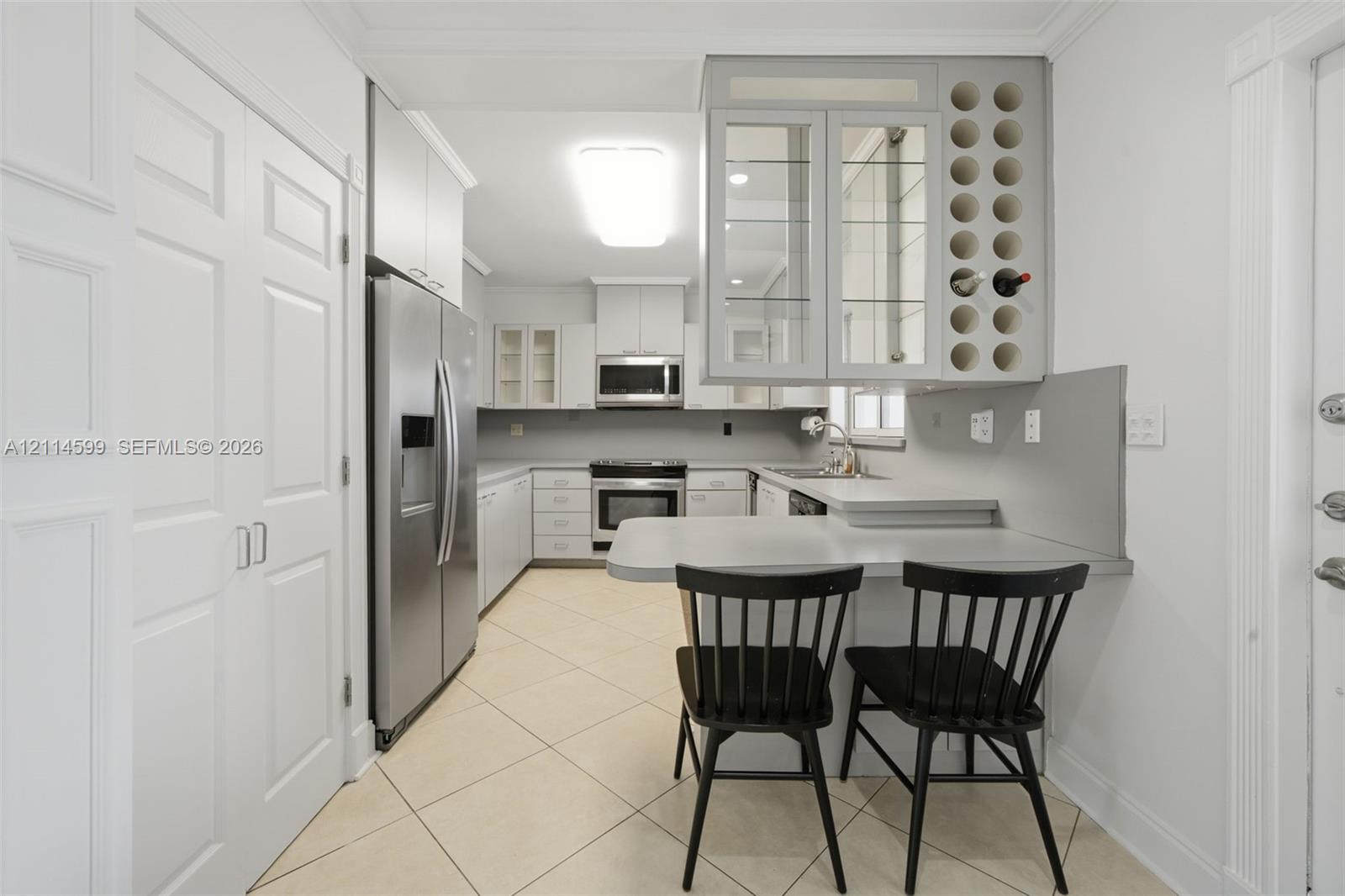 Kitchen featuring shaker-style cabinetry, built-in wine storage, solid-surface countertops, stainless steel appliances, and tile flooring