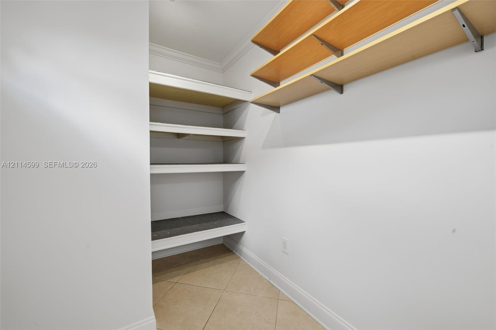 Storage area featuring white-finished built-in shelving, natural wood-tone open shelving with metal brackets, and tile flooring