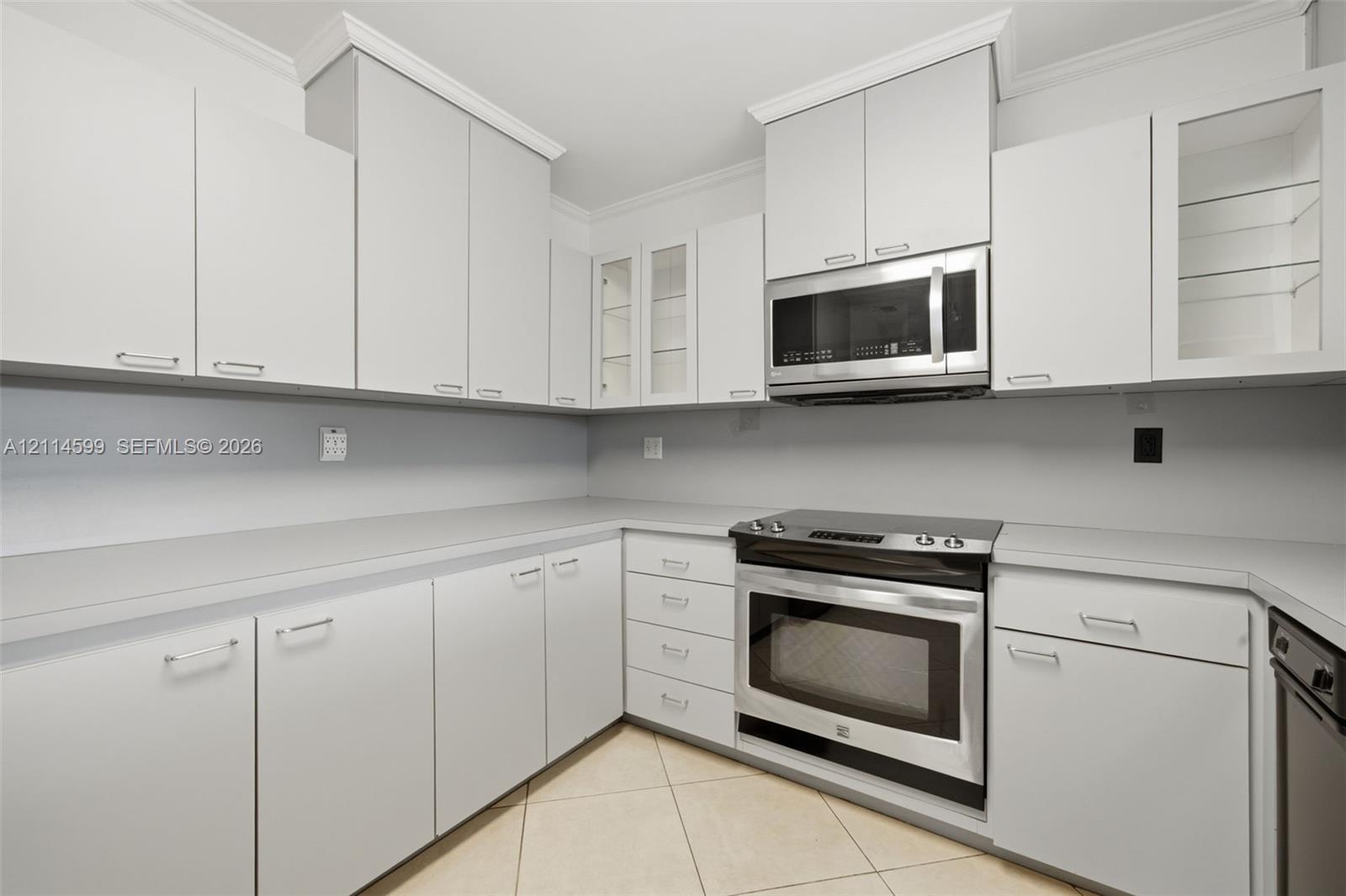 Kitchen featuring white cabinetry with crown molding, glass-front upper cabinet displays, solid-surface countertops, built-in stainless steel microwave, and stainless steel slide-in electric range