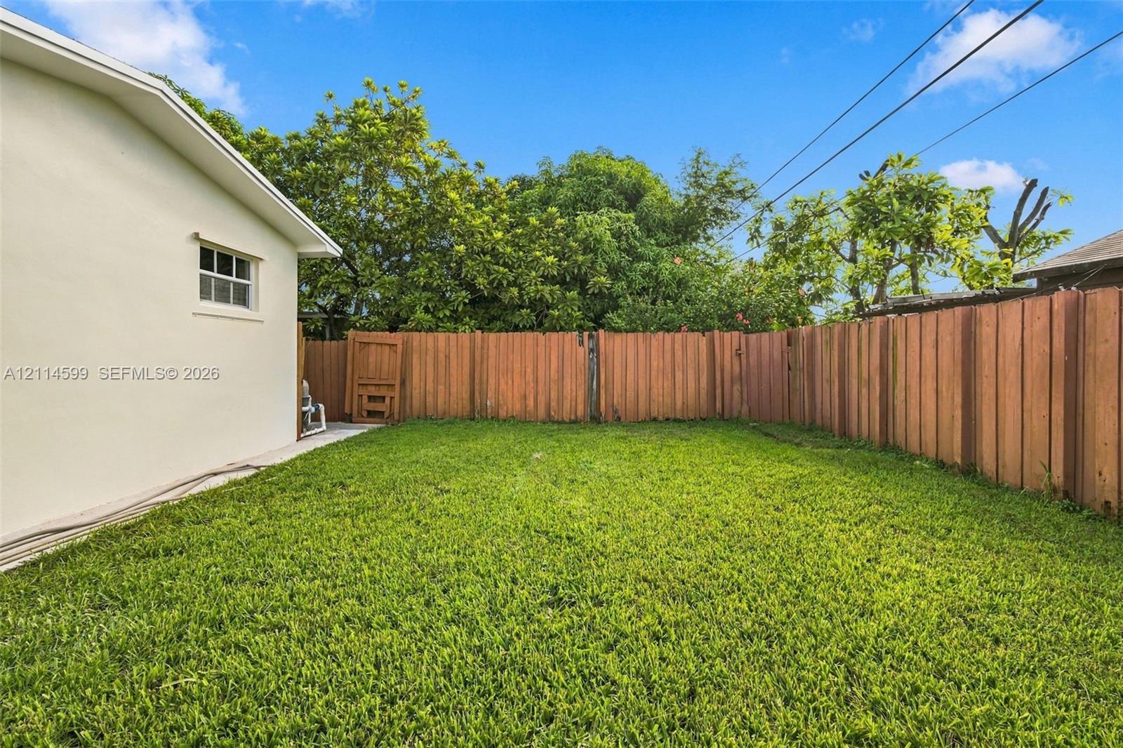 Backyard featuring a manicured lawn, perimeter wood fencing, and mature trees
