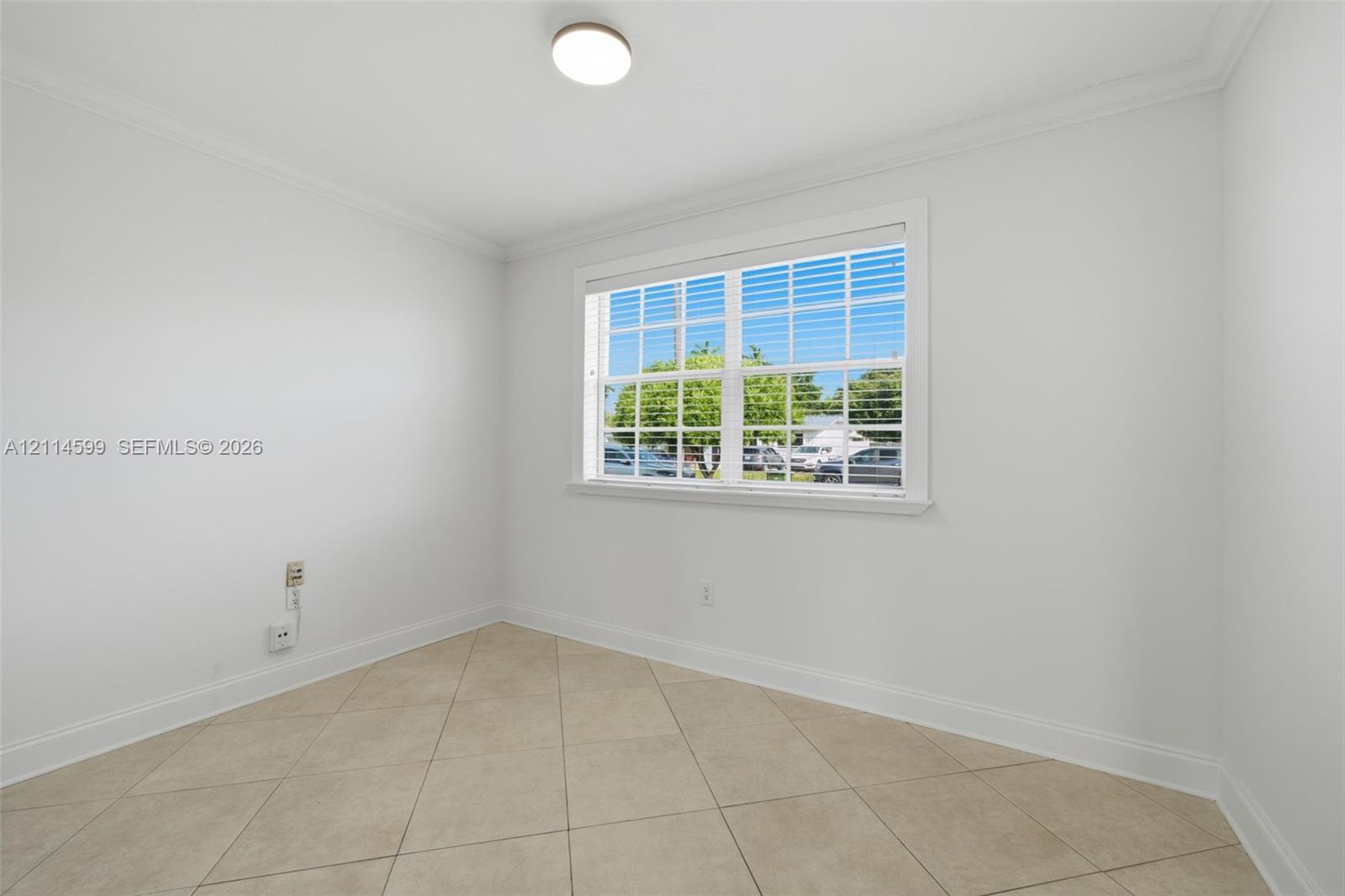 Interior room featuring neutral wall paint, large format tile flooring, crown molding, and a multi-pane window with interior blinds