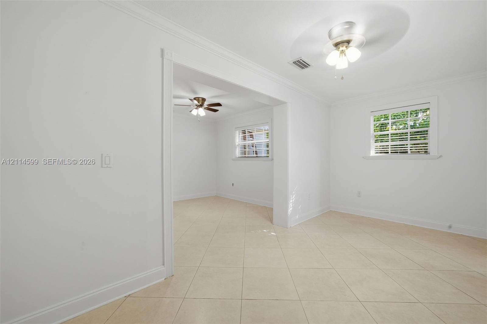 Neutral-toned tile flooring, crown molding, and two ceiling-mounted light fixtures with integrated fans