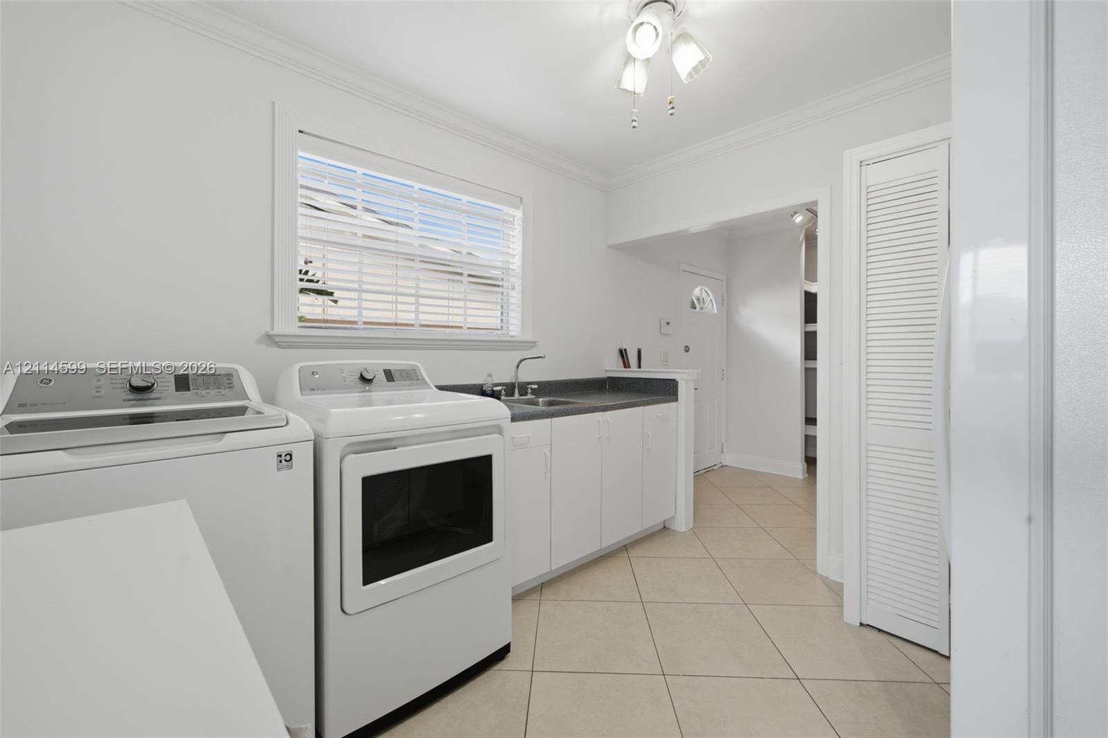 Utility area featuring tile flooring, white cabinetry, a countertop with a built-in sink, and louvered closet doors