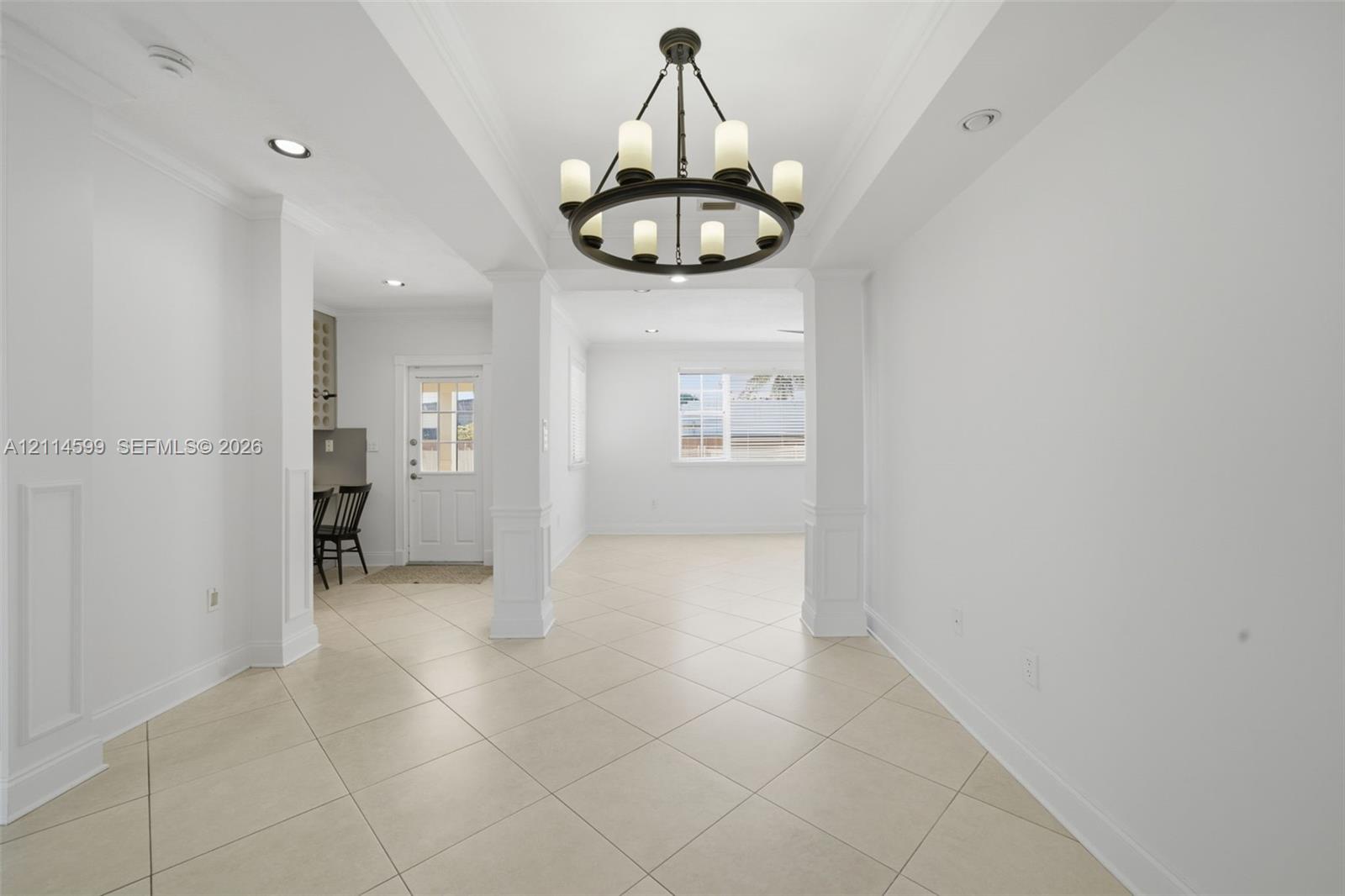 Interior featuring tile flooring, crown molding, structural columns with wainscoting detail, and a prominent circular multi-light chandelier