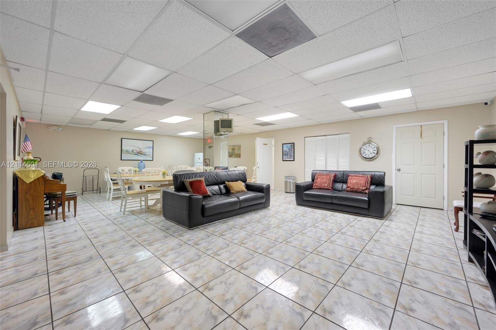Large open-concept space featuring grid-pattern tile flooring, suspended drop ceiling, and inset panel lighting