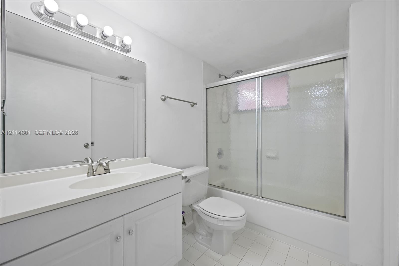 Bathroom featuring a white vanity with an integrated sink, full-width wall mirror, four-bulb vanity lighting fixture, and a tub-shower combination enclosed by textured glass sliding doors