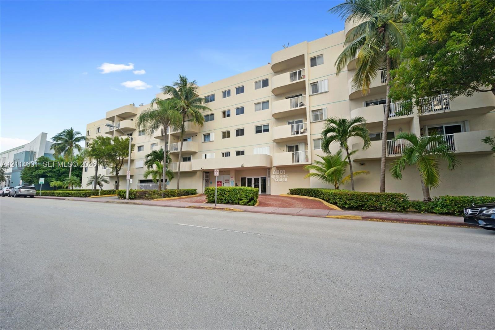 Multi-story residential building featuring private balconies, stucco exterior, and mature palm tree landscaping