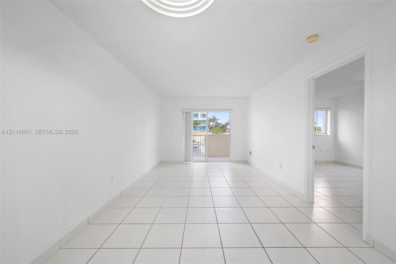 Interior space featuring white ceramic tile flooring, neutral wall finishes, and glass sliding doors leading to an exterior balcony