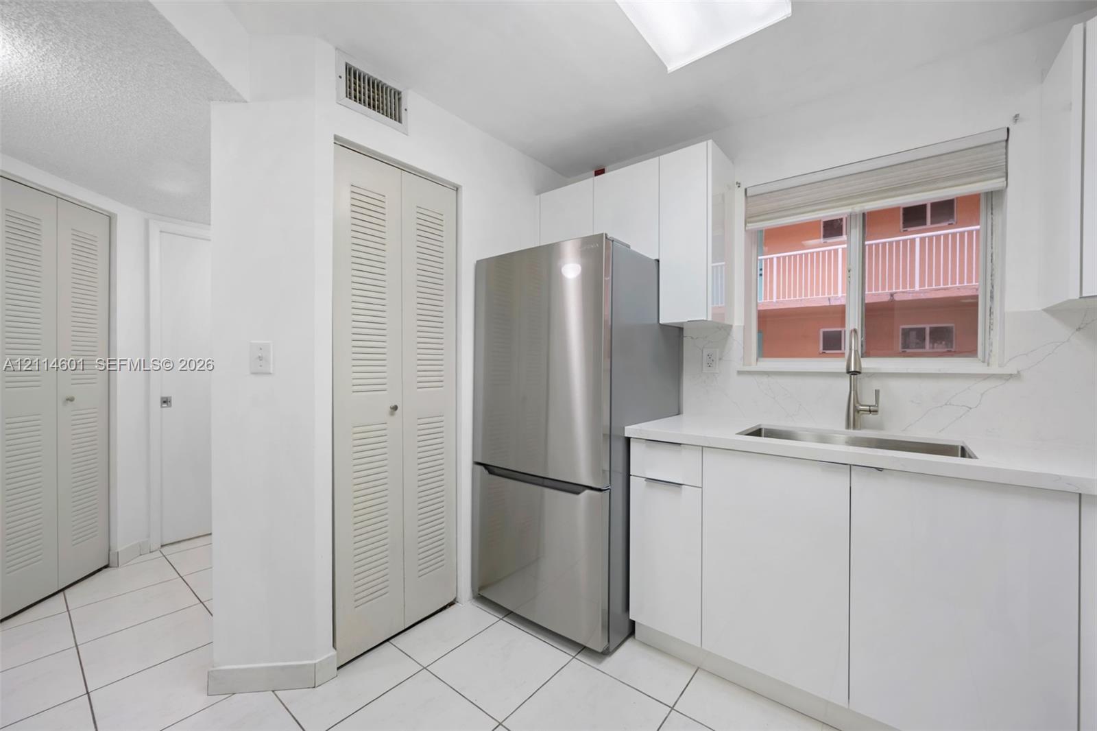Kitchen featuring white cabinetry, stainless steel refrigerator, stone-composite countertop, undermount stainless steel sink with pull-down faucet, and white tile flooring