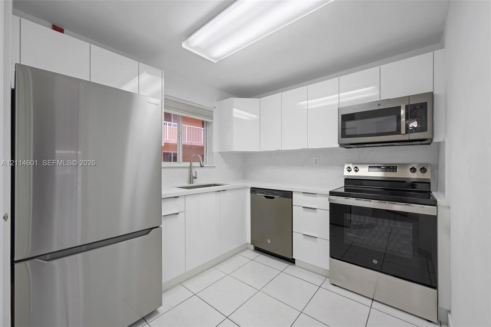 Kitchen featuring high-gloss white cabinetry, white stone-finish countertops, stainless steel appliance suite, and light-toned floor tile