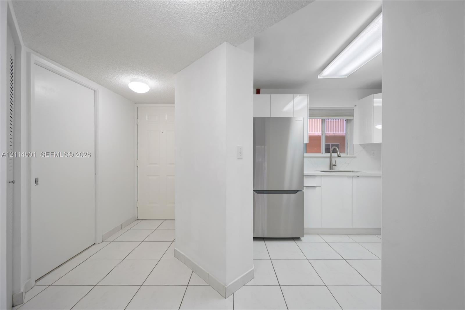 Kitchen featuring white cabinetry, stainless steel refrigerator, undermount sink, and white tile flooring