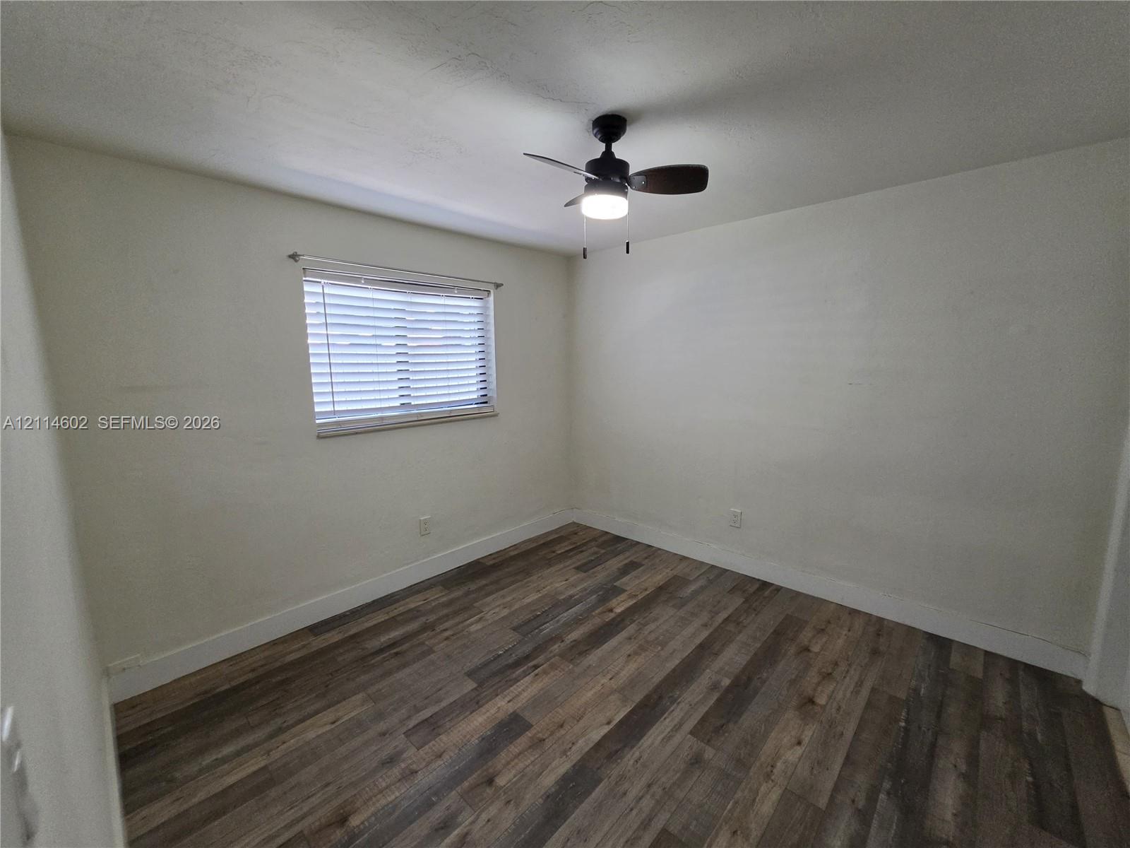 Interior room featuring wood-finish flooring, a neutral wall palette, a single window with horizontal blinds, and a ceiling-mounted fan with light fixture